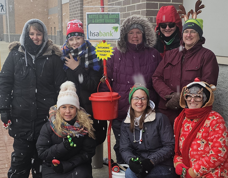 HSA Bank volunteers dressed in winter clothing posing outside with a Salvation Army red bucket